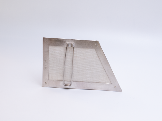 Rückseite einer unregelmäßig-eckigen Brosche mit einem Rahmen aus Silber und Leinwand in bunten feinen Streifen, sie sieht aus wie ein Bilderrahmen