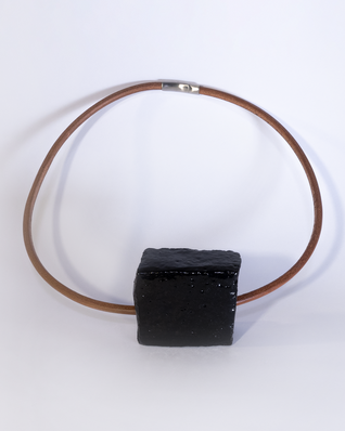Anhaenger aus einem quadratischen schwarz glasierten Keramikstück an einem schweren rötlichen Lederband