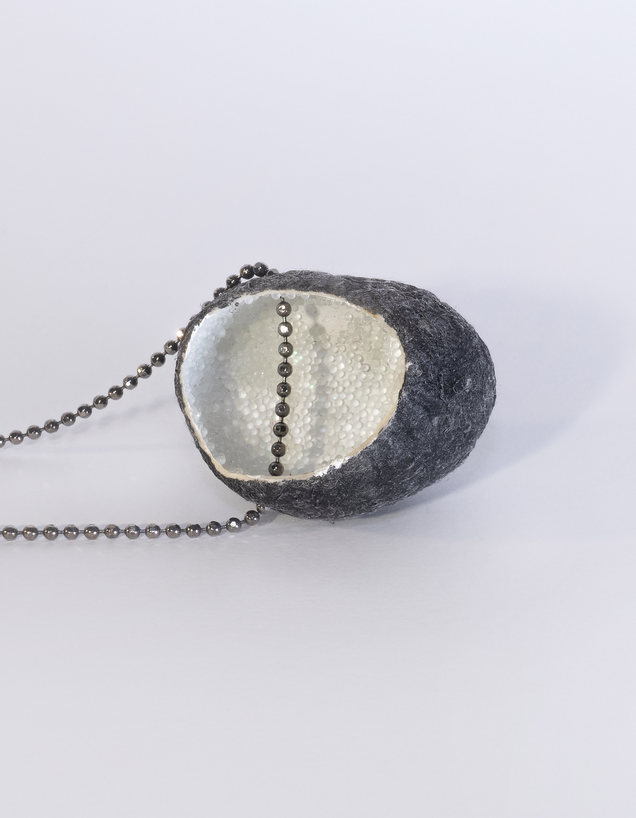 Halskette mit einem offenen, außen schwarzen, innen permuttweißen Seidenkokon Anhaenger, innen ist Reflektionsgranulat, die Kette ist aus Silber 