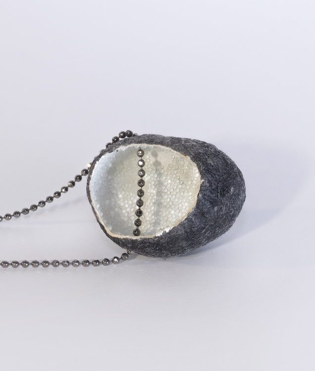 Necklace with an open silk cocoon pendant, black on the outside, pearlwhite on the inside, inside is reflective granulate, the chain is made of silver