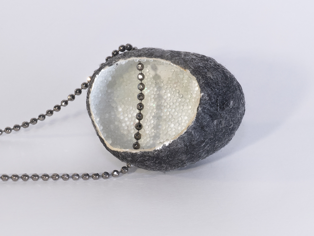 Necklace with an open silk cocoon pendant, black on the outside, pearlwhite on the inside, inside is reflective granulate, the chain is made of silver