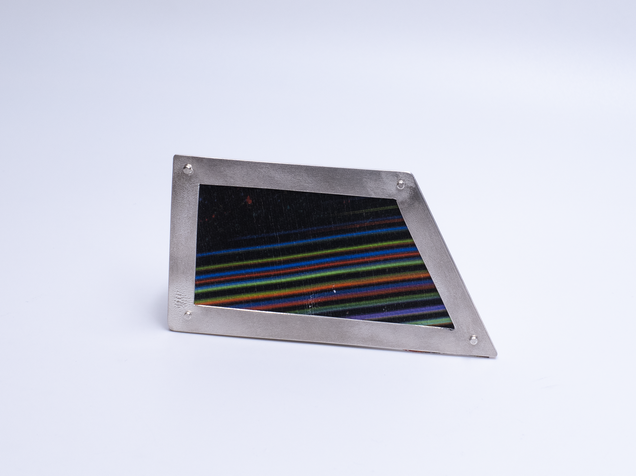 Unregelmäßig eckige Brosche mit einem Rahmen aus Silber und Leinwand in bunten feinen Streifen, sie sieht aus wie ein Bilderrahmen