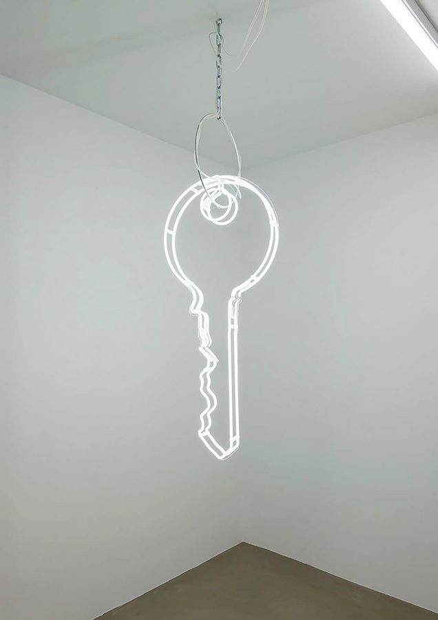 Big white neon key on steel chain is hanging down from the ceiling of a white room