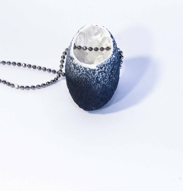 Halskette mit einem schwarzen Seidenkokon Anhaenger, dessen weißes Inneres mit kleinen Glaskugeln gefüllt ist, die Kette ist aus Silber