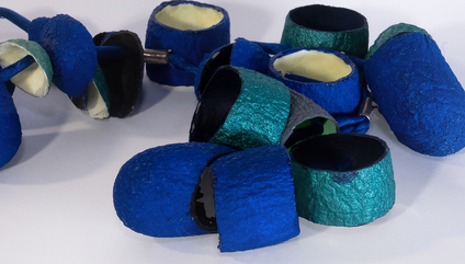 Viele offene Seidenkokons, die in leuchtenden Blautönen und mit Nachtleuchtpigment bemalt sind, an einem blauen seidenen Band