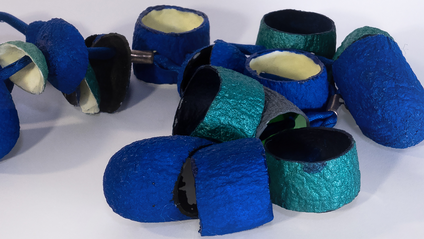 Many open silk cocoons painted in bright shades of blue and night luminescent pigment on a blue silk ribbon