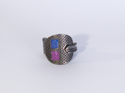 Silberner Schlüssel, der zu einem Ring gebogen ist, zwei rechteckige Flächen sind mit dunkelviolettem und pink Emaille gefüllt