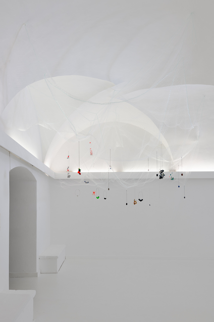 In the exhibition Mulberry Tubes, jewellery artist Michaela Rapp presents coloured cocoon necklaces from the IMAGO collection inside a see-through net hanging down from the ceiling as if they were floating.