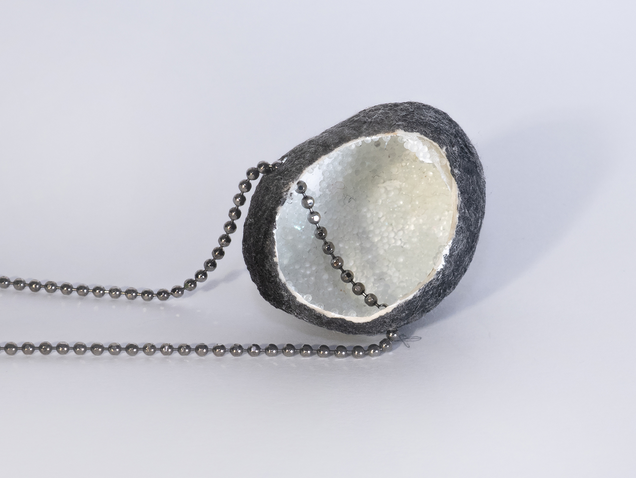 Necklace with an open silk cocoon pendant, black on the outside, pearlwhite on the inside, inside is reflective granulate, the chain is made of silver