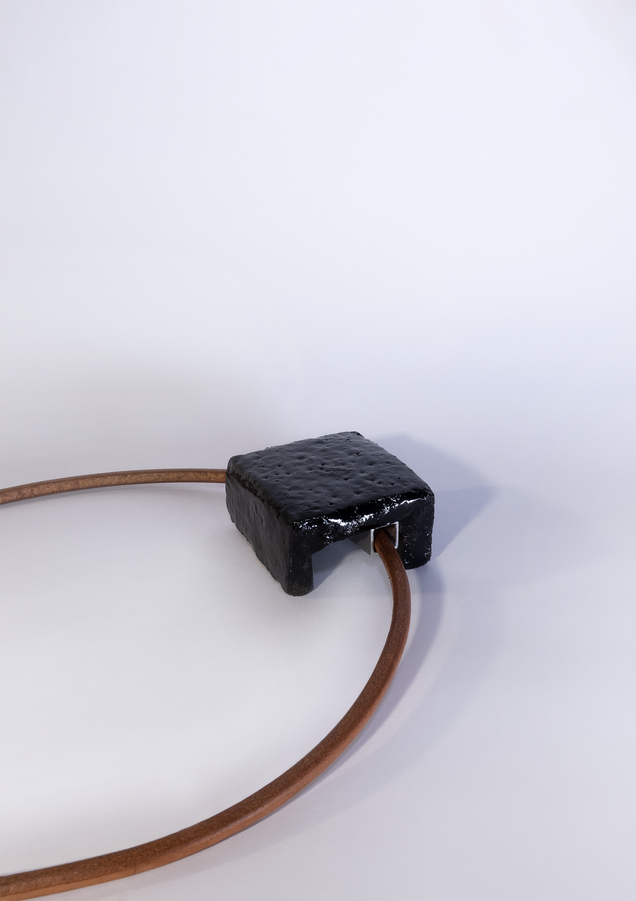 Pendant made of a square black glazed ceramic piece on a heavy reddish leather strap