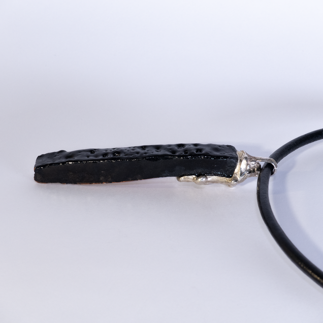 Pendant made of an elongated black glazed ceramic piece with a silver cap, the glaze "Fat Lava" looks like the surface of the moon 