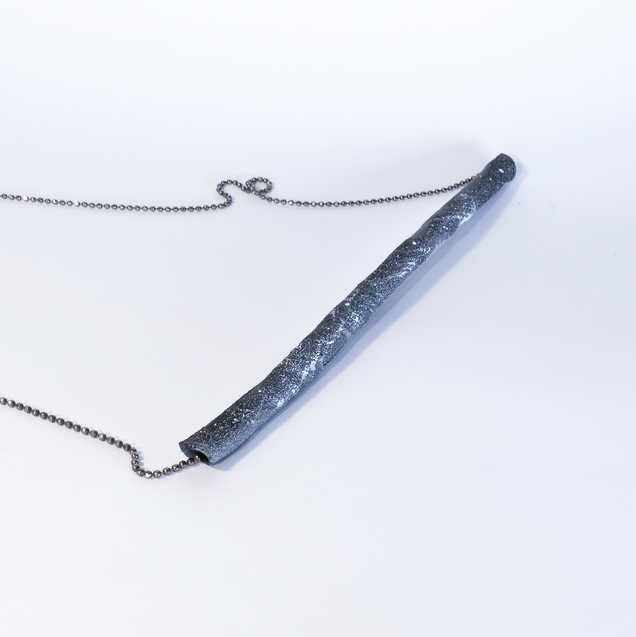 Silver necklace with a black tube, looking like a piece of coal
