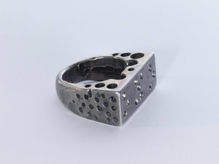 Silver ring showing dimples in braille on the upper surface, the other parts of the ring are perforated