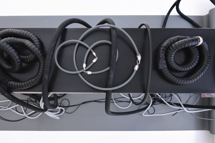 In der Ausstellung Mulberry Tubes zeigt die Schmuckkünstlerin Michaela Rapp eine Installation aus schweren und dünneren schwarzen und grauen Halsketten, die auf einer niedrigen Bank liegen; diese steht auf grauem Papier, das die Wand und den Boden bedeckt.