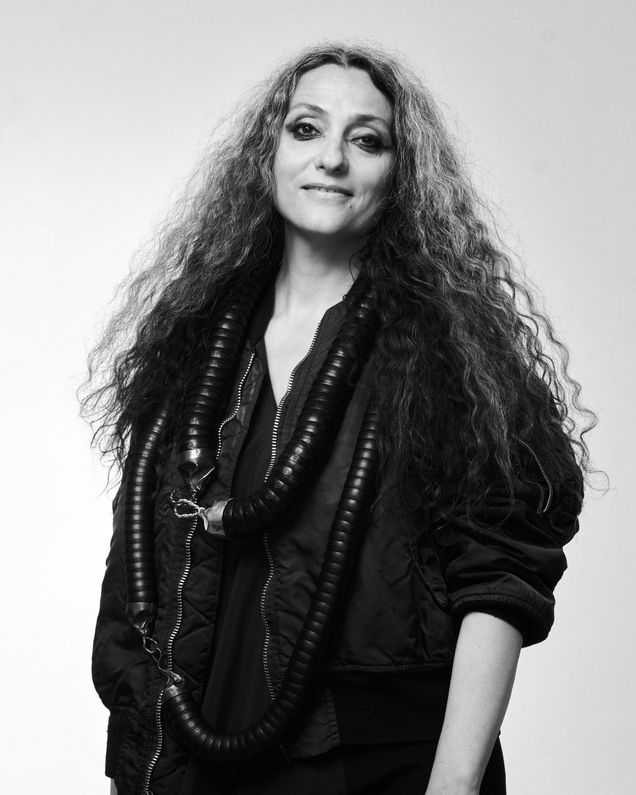 Artist Maja Vukoje wears two heavy tube necklaces from the BRAZIL collection over a black blouson, her hair is long and she smiles