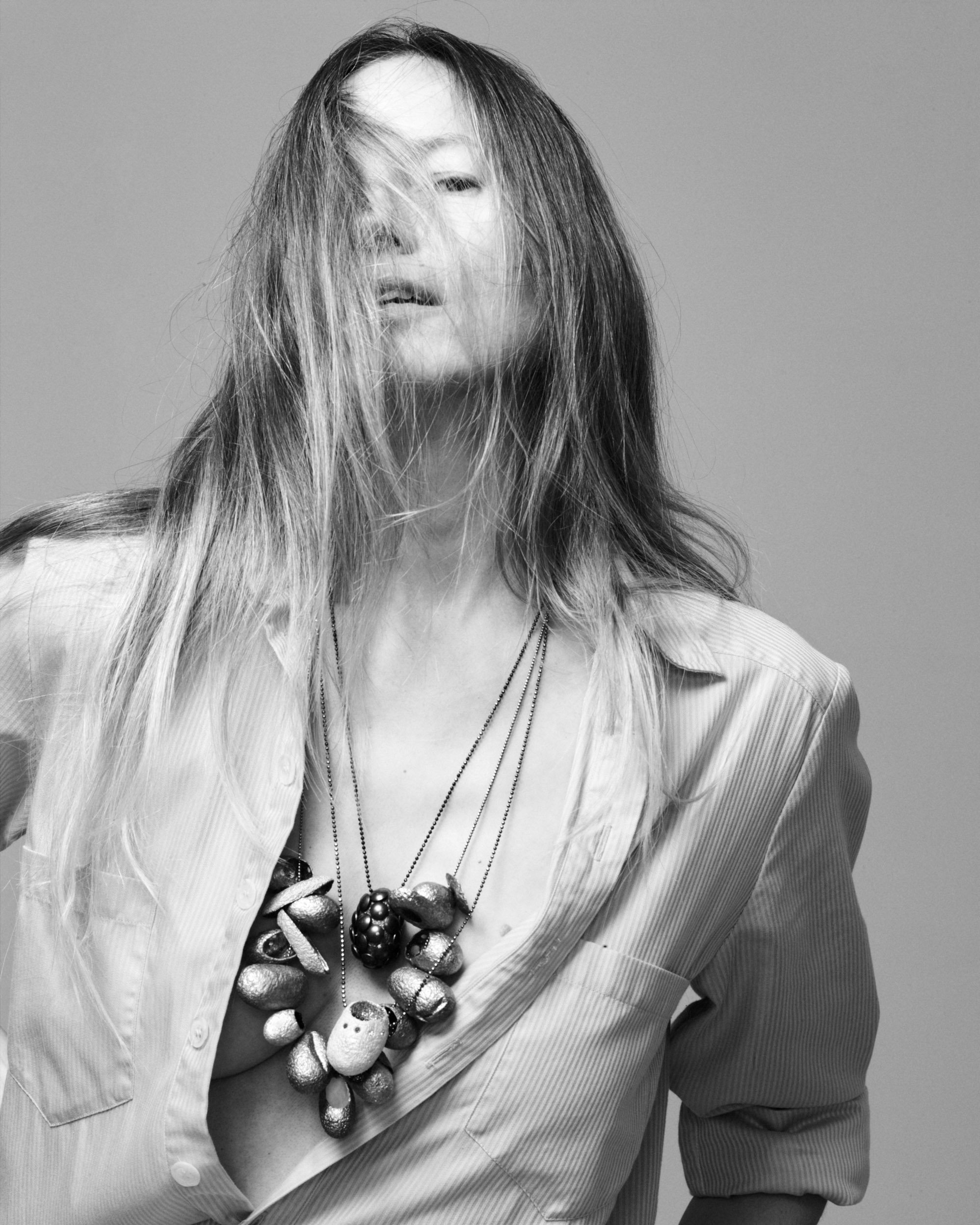 Künstlerin Michaela Schwarz–Weismann trägt viele Seidenkokon–Ketten über einem hellen Hemd, ihre langen Haare verdecken ihr Gesicht