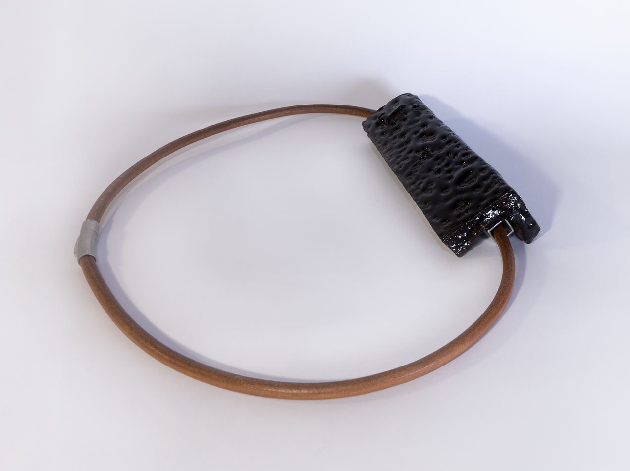 Anhaenger aus einem rechteckigen schwarz glasierten Keramikstück an einem schweren rötlichen Lederband
