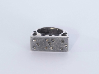Silberner Ring, der auf der oberen Fläche Vertiefungen in Brailleschrift zeigt, die anderen Teile des Rings sind durchlöchert