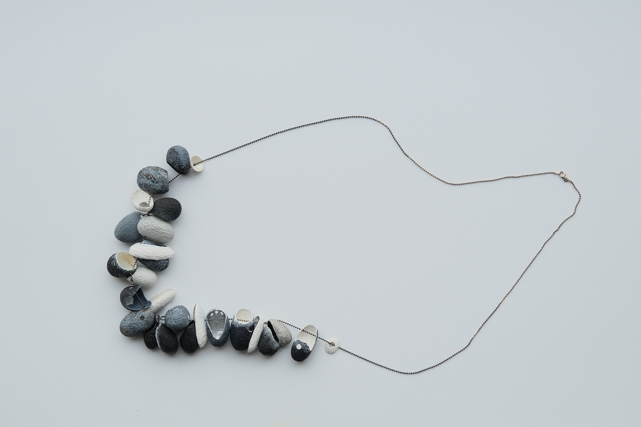 Long silver necklace with 19 threaded silk cocoons open at the front, painted on the outside in shades of grey, black and white