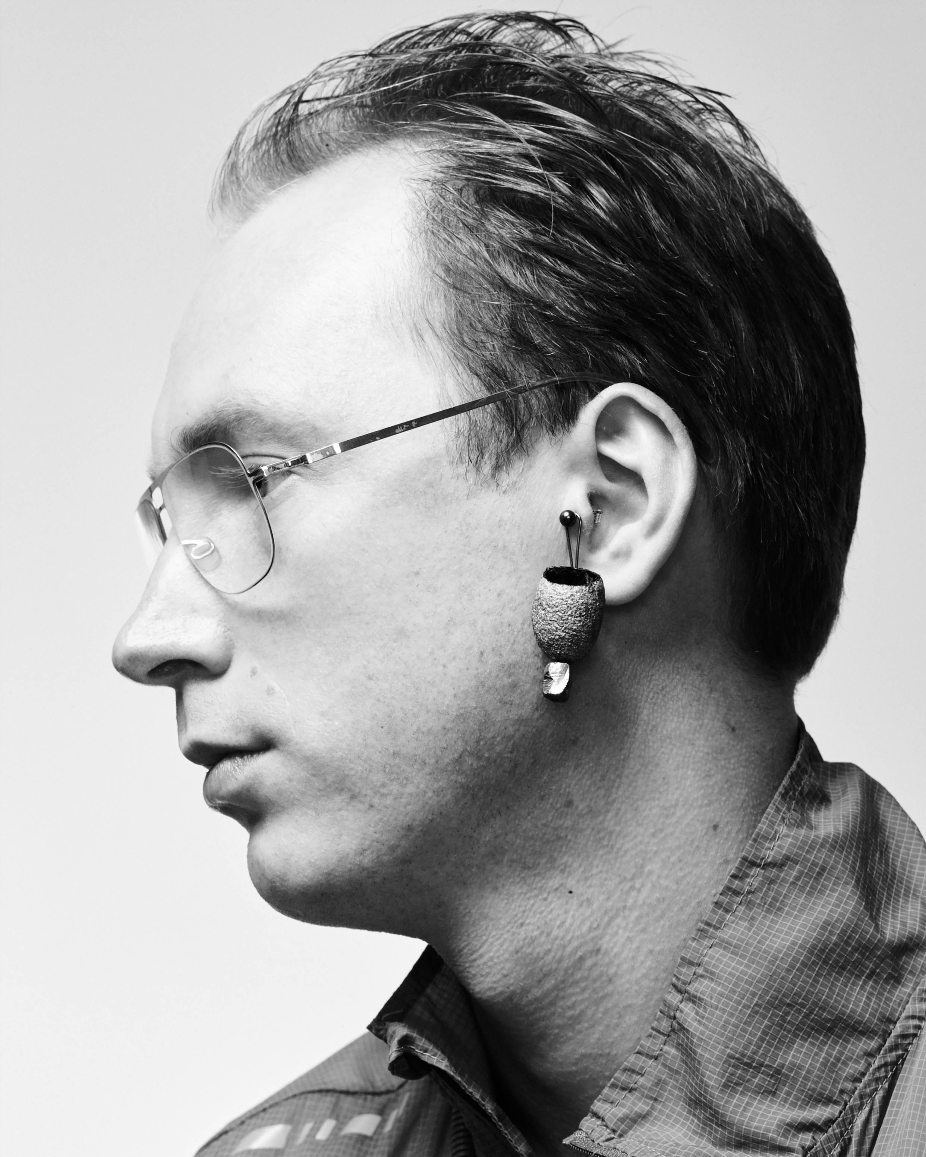 Portrait des Künstlers Alexander Jackson Wyatt mit  IMAGO Ohrring mit Silicium Nugget, er trägt einen grauen Blouson und eine Brille